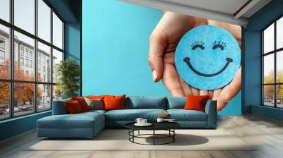 smiling blue paper face with cute eyelashes held by hands on turquoise background, free space for text, world health day  concept  Wall mural