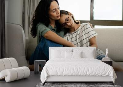 Caring mother comforting her teenage daughter, both sitting on the couch at home, sharing a tender and supportive moment Wall mural