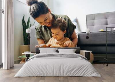 Mom reading a book with baby boy at home. Early age children education, development. Mother and child spending time together. Candid lifestyle. Wall mural