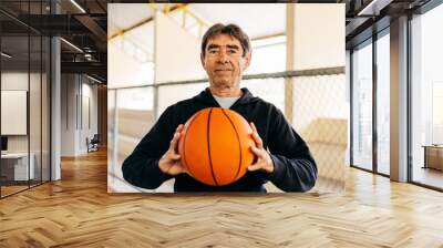 Physical activity in old age. Portrait of elderly man playing basketball Wall mural