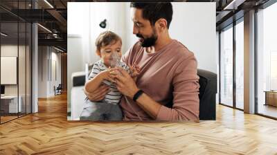 Portrait of a baby boy inhaling medicine in nebulizer with his father at home. Wall mural