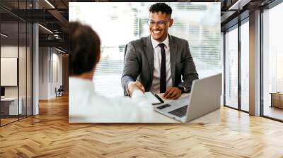 Sealing a deal. Close-up of two business people shaking hands while sitting at the working place Wall mural