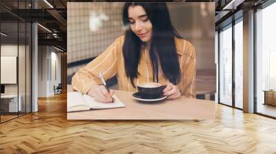 Pretty woman in urban cafe write book with laptop and black coffee Wall mural