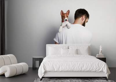 Handsome man snuggling and hugging his basenji puppy dog, close friendship against a white background Wall mural