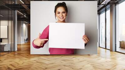 Pretty smiling woman holding empty blank board isolated on the gray background Wall mural