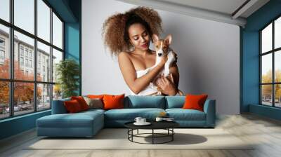 Pretty young black american african girl embracing puppy on white background. Studio portrait of white appealing female chilling with dog on white background Wall mural