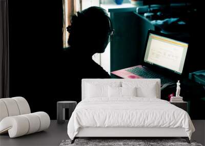 Woman working on a laptop in a dark room. Woman with glasses uses laptop for work Wall mural