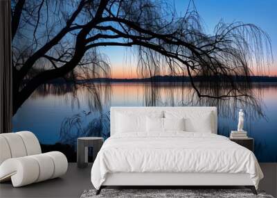 A silhouetted willow sways gently over a serene lake at dusk, creating a tranquil, picturesque scene. Wall mural