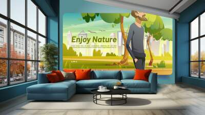 Enjoy nature banner with man walking in city park with green trees and grass. Vector landing page with cartoon illustration of character with beard walks in public garden with town on skyline Wall mural