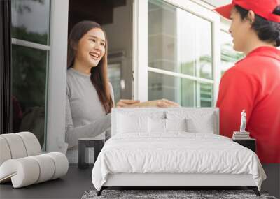 Delivery service asian young customer woman hand received cardboard box parcel from messenger male. Postman in red uniform holding cardboard box parcel, carton send to client at home, shopping online. Wall mural