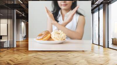 Diet concept, asian young woman hand push out, deny sugar donut, doughnut and sweet taste food on plate, fighting to keep it from getting fat when person bring to me. Healthy nutrition of weight loss. Wall mural