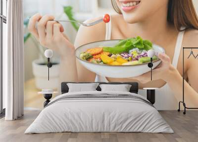 Diet concept, happy asian young woman hand use a fork to prick tomato, fresh vegetable or green salad, eat nutrition food  on table at home, low fat to good body. Girl getting weight loss for healthy. Wall mural