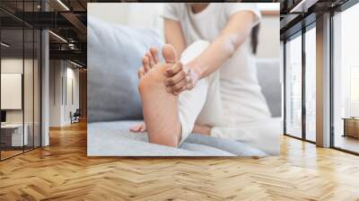 Foot pain concept, close up hand of young woman rubbing, massaging sore feet area of pain, girl suffering on sofa, couch at home. Discomfort painful feet ache from walking for long. Physical injury. Wall mural