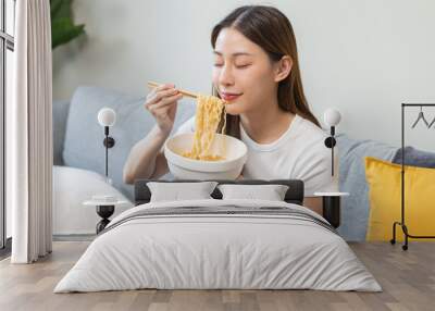 Happy temptation, cute asian young student woman, girl using chopsticks eating instant ramen, noodles soup in bowl while watching TV in living room at home, cooking meal fast food lifestyle of person. Wall mural