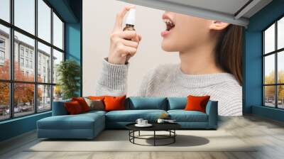 Health care treatment sore throat concept, sick pain asian young woman have cough symptom holding medicine bottle, using spray in mouth to protect disease from bacteria, illness from virus infection. Wall mural