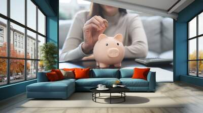 Saving money wealth concept, asian young business woman hand putting coin into piggy for saving cost, cash finance planning to spend enough money on her income for save money, payment tax, investing. Wall mural