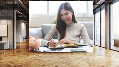 Saving money wealth concept, asian young business woman hand write management budget for saving cost, cash finance planning to spend enough money on her income for save money, payment tax, investing. Wall mural