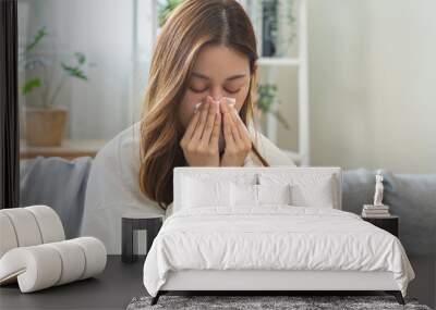 Sick, coronavirus or covid, tired asian young woman have a fever, flu and hand in use tissues paper sneezing nose, runny while sitting on sofa, couch at home. Health care with disease, pandemic virus Wall mural