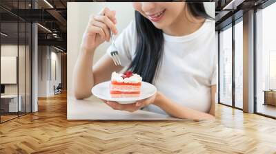 Smiling happy asian young woman holding fork eating slice piece chiffon strawberry layer cake sitting at table, girl eat sweet or dessert cake. Enjoying healthy fast food unhealthy choice concept. Wall mural