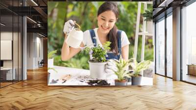 Spring hobby, happy asian young woman hand holding watering can in flowerpot, houseplant with dirt or soil on table at home, taking care gardening plant in garden, green tropical, beauty and nature. Wall mural