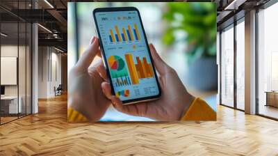 Mobile Analytics: A close-up shot of hands holding a smartphone displaying a data dashboard with charts and graphs, showcasing modern business analysis and data-driven decision making. Wall mural