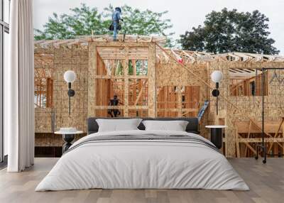 New residential home construction in framing stage, workman on the roof rafters looking at building plans, OSB, oriented strand board, sheathing on exterior walls with window holes cut out
 Wall mural