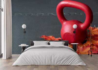 Red iron kettlebell on a black rubber gym floor, with orange and yellow maple leaves, fall fitness Wall mural