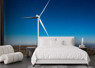 White wind turbine on a hill top, in a dry landscape with more turbines and blue sky in background Wall mural