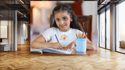 Beautiful child girl drawing and posing towards camera - studio isolated  childhood  girl studying. Stock image of an Indian kid dressed in casual wear is drawing and studying at home - facing came... Wall mural