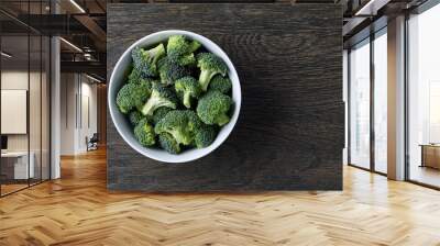 Fresh green broccoli in a white bowl on dark wooden background, top view Wall mural