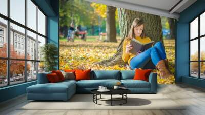 Pretty woman sitting and reading book in the autumn park Wall mural