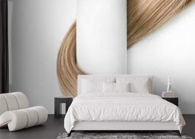 A strand of blond hair with a bottle of shampoo on a white background. Close-up. Wall mural