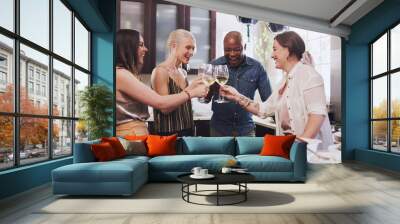 Group of friends, toast and cooking in kitchen with wine, prepare a festive meal and relax together. Diversity, people and alcohol for happiness, party and at home for holiday, champagne and food. Wall mural