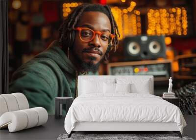 African american  Music producer in a recording studio wearing headphones and orange glasses, adjusting sound equipment with a focused expression Wall mural