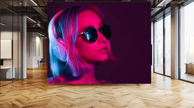 Mysterious hipster teenager in sunglasses listening to music with headphones. Portrait of millennial pretty girl with short hairstyle with neon light. Dyed blue and pink hair. Wall mural