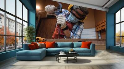 Carpenter hand with chisel in hand working on carpentry. Carpenter wearing safety equipment while chiseling and making wooden products in a home workshop. Wall mural