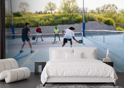 Multiracial group playing pickleball doubles on blue court, sunny day Wall mural