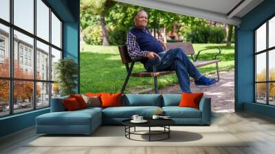 Relaxed senior man sits on a park bench, surrounded by trees, in casual attire and a contented expression Wall mural