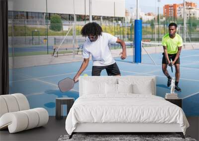 Two African teammates strategizing and enjoying a fun game of pickleball on a bright, sunny day. Wall mural