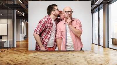 One man shares a secret or whispers gossip in the ear of another person who is looking thoughtfully at the top. Wall mural