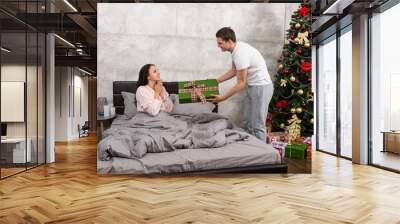 Young man giving a present to his happy girlfriend, while she si Wall mural