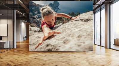 Brave young woman climber fearlessly climbs up sheer stone wall in mountains, overcoming obstacles. Dangerous chasm balancing, adrenaline and courage in extreme sports Wall mural