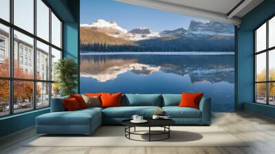 A tranquil lake surrounded by dense forest and snow-dusted mountains, the mirror-like water perfectly reflecting the natural beauty of the scene under a clear winter sky Wall mural