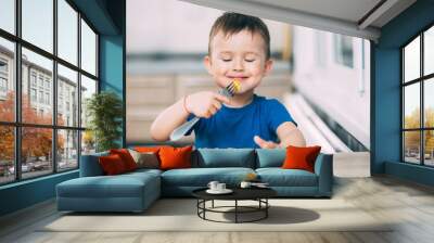 a child in a t-shirt in the kitchen eating an omelet, a fork Wall mural