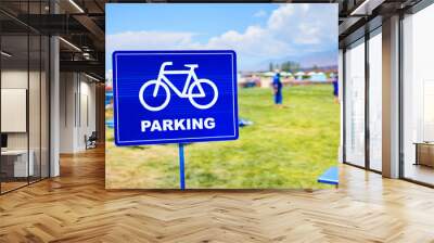 A traffic sign in blue with a bicycle symbol indicating parking, set against a backdrop of grassland and a clear blue sky. A serene landscape perfect for recreation Wall mural