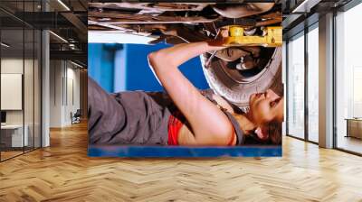 Sexy mechanic girl lying under the car and repairing it. Side angle Wall mural