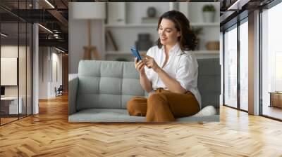 woman is using a phone sitting on a sofa Wall mural