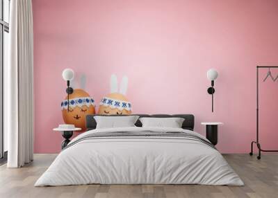 Two little easter eggs with a painted drawn rabbit faces and ears on them in laying on the pink table isolated. Easter holidays decorations, preparations concept. Holy religious day. Copyspace. Wall mural