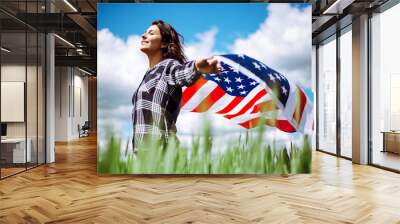 Young woman waves an american flag on the green wheat field. Patriotic holiday celebration. United States of America independence day, 4th of July concept. Wall mural