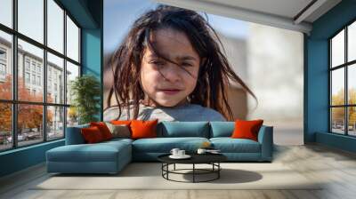 A portrait of a beautiful little roma girl with unwashed hair on blurred background in a Roma settlement Wall mural